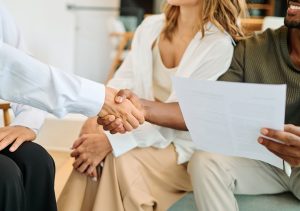 Young happy couple and an agent in a new property shaking hands or with advisor in office